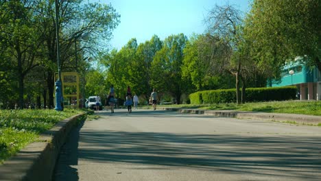 Sonniger-Tag-Am-Jarun-See,-Zagreb,-Mit-Fußgängern,-Die-Einen-Von-Bäumen-Gesäumten-Weg-Genießen
