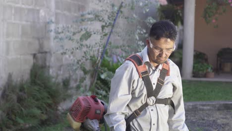 Hispanic-adult-man-using-a-weed-trimmer-to-work-in-gardening