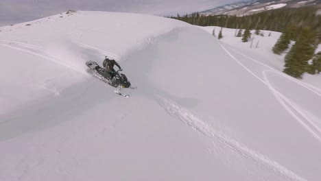 Aerial-FPV-Flying-Over-Snow-Covered-Hillside-Near-Sharkstooth-Peak-With-Snowmobile-Rider-Riding-Over-The-Top