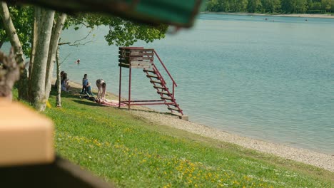 Tranquilidad-Junto-Al-Lago-En-El-Lago-Jarun,-Con-Una-Torre-De-Salvavidas-Y-Gente-Disfrutando-De-Un-Día-Soleado.