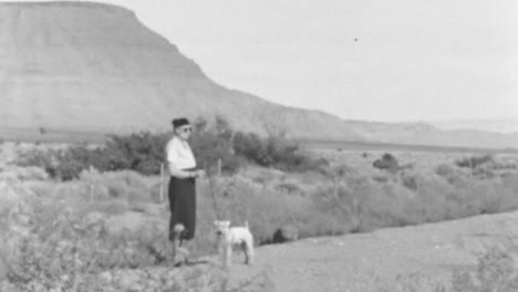 Woman-in-Vintage-Clothes-Walks-Dog-in-Distant-Landscape-Surrounded-by-Mountains