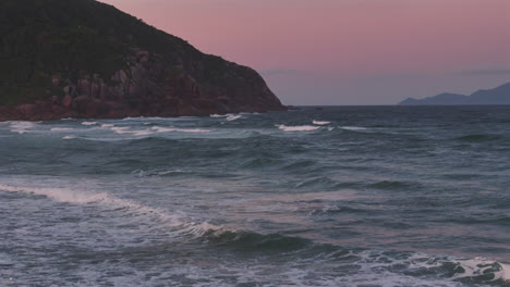 Olas-Rompiendo-En-La-Playa-Brava-Con-Un-Telón-De-Fondo-De-Montañas-Rocosas-Durante-Una-Impresionante-Puesta-De-Sol