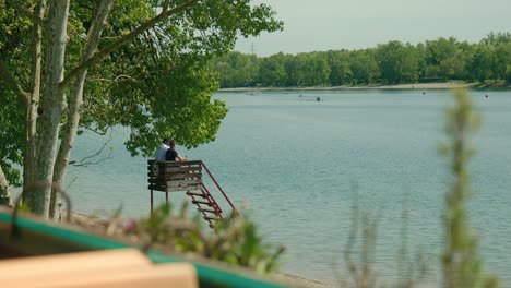 Serene-moment-by-Jarun-Lake,-with-people-on-a-wooden-dock-amidst-calm-waters-and-lush-trees