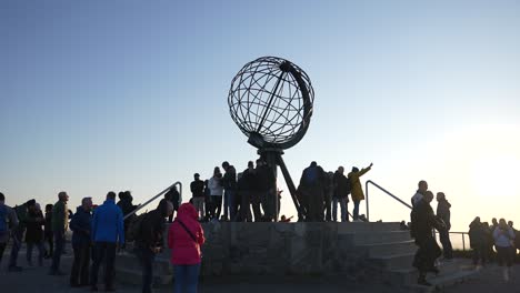 Multitud-De-Personas-Bajo-El-Monumento-Del-Globo-En-El-Cabo-Norte-De-Noruega-Al-Atardecer,-Cámara-Lenta