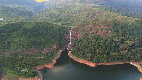 Impresionante-Toma-De-Drones-De-Las-Cataratas-Gartmore-En-Sri-Lanka,-Con-Exuberante-Vegetación,-Arenas-En-Tonos-Naranjas-Y-Rocas-Contra-Un-Cielo-Azul-Intenso.