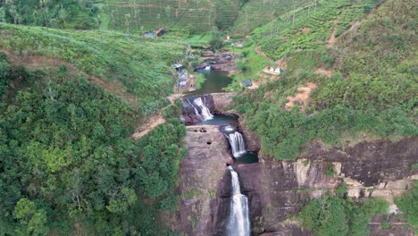 Atemberaubende-Drohnenaufnahme-Der-Gartmore-Falls-In-Sri-Lanka,-Mit-üppigem-Grün,-Orangefarbenem-Sand-Und-Felsen-Vor-Einem-Strahlend-Blauen-Himmel
