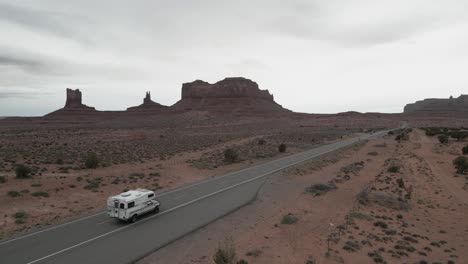 A-camper-truck-traverses-the-road-amidst-the-desolate-and-barren-expanse-of-Utah's-Monument-Valley-National-Park,-embodying-the-essence-of-van-life,-a-journey-of-freedom
