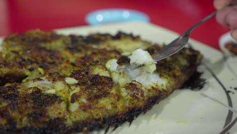 Close-up-of-grilled-fish-being-flaked-with-a-fork,-served-on-a-plate,-dining-experience,-indoors