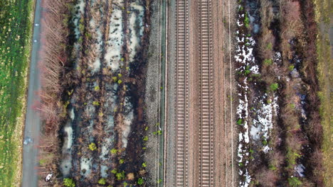 Dual-Railway-Tracks-in-Winter,-Bordered-by-Snowy-Patches-and-Greenery,-Aerial-View