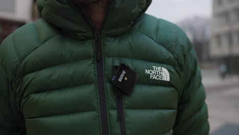 Close-up-of-compact-wireless-Rode-microphone-attached-to-green-jacket