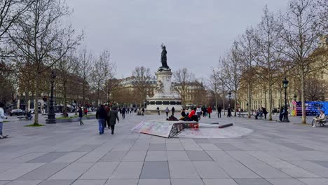 Place-De-La-République-En-París-Con-Gente-Caminando-Y-Una-Rampa-Para-Patinetas,-Día-Nublado