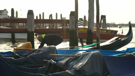 Person-Uncovers-Floating-Gondola-strapped-to-wooden-pole-in-Venice-early-in-the-morning
