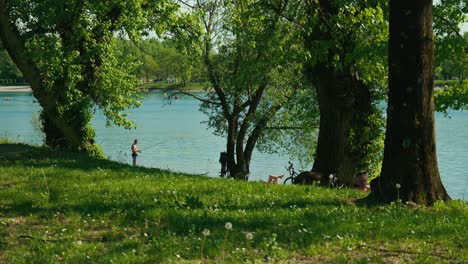 Serene-Jarun-Lake,-with-individuals-fishing-and-resting-under-lush-trees