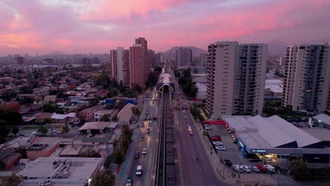 Aerial-view-tracking-the-Santiago-subway,-passing-through-the-exterior,-subway-station-at-altitude,-epic-sunset-in-the-background,-Santiago's-main-means-of-transportation