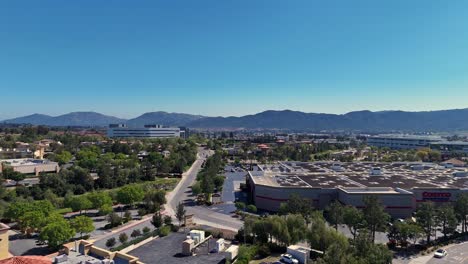 Vuelo-De-Drones-A-Lo-Largo-Del-Paseo-Marítimo-Detrás-De-Costco-En-Temecula,-California,-Desde-Detrás-Del-Almacén-Hasta-El-Estacionamiento-Lateral-Con-árboles-Y-Edificios-De-Oficinas-Vecinos-Y-Colinas-Al-Fondo