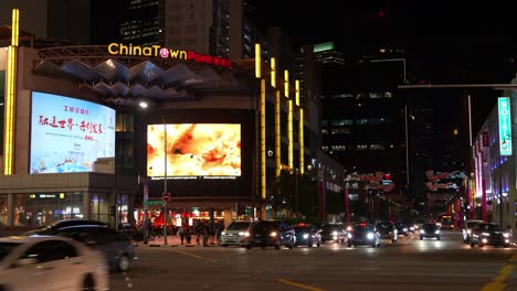 Busy-night-traffics-at-the-junction-of-New-Bridge-Road-and-Upper-Cross-Street-featuring-landmark-Chinatown-Point-shopping-mall,-Singapore,-static-shot