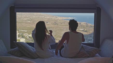 young-man-walks-room-with-beautiful-view,-woman-leans-into-him-as-a-romantic-gesture
