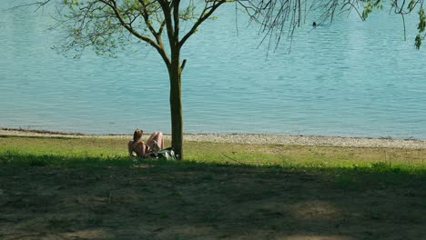 Relajación-Tranquila-Junto-Al-Lago-Jarun,-Zagreb,-Mientras-Una-Mujer-Joven-Disfruta-De-Un-Retiro-Soleado-Junto-Al-Lago