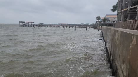 This-is-a-short-video-clip-of-ocean-waves,-crashing-onto-a-concrete-pier-with-wooden-docks-and-homes-in-the-background,-during-an-afternoon-storm