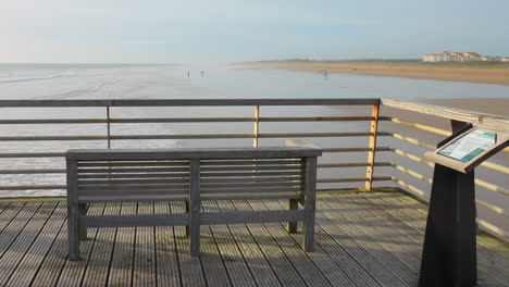 Leere-Holzbank-Mit-Blick-Auf-Einen-Ruhigen-Strand-In-Saint-Jean-de-Monts-Bei-Tageslicht,-Klarer-Himmel