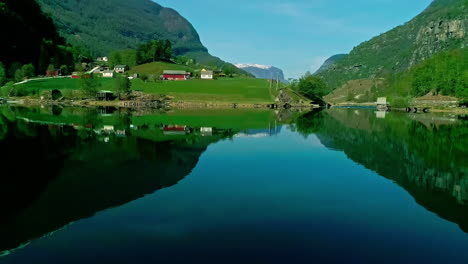 Drohnenaufnahme-Der-Atemberaubenden-Küste-Norwegens,-Des-Dorfes-Flam,-Des-Fjords-Und-Der-Grünen-Hügel,-Spiegelungen-Auf-Dem-Wasser-An-Einem-Sonnigen-Tag