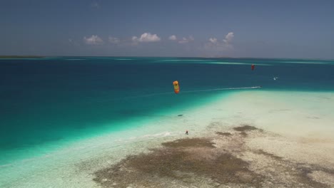 A-yellow-kite-surfer-gliding-over-the-crystal-clear-waters-of-los-roques,-venezuela,-aerial-view