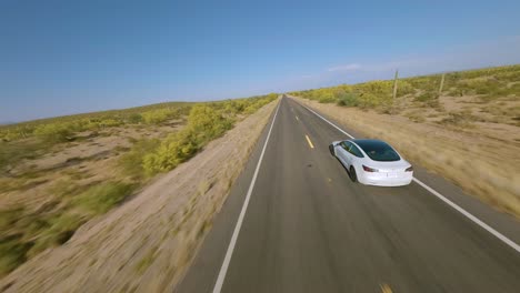 Aerial-FPV-Following-White-Tesla-Model-3-Driving-Along-Desert-Highway-In-Florence,-Arizona