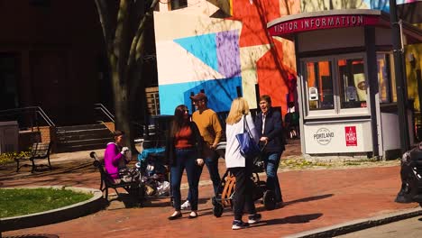 Older-woman-pushing-a-baby-stroller-in-a-Portland,-Maine-park-with-the-baby's-parents