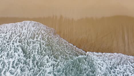 A-frothy-wave-cresting-onto-sandy-beach,-capturing-nature's-calm,-aerial-view