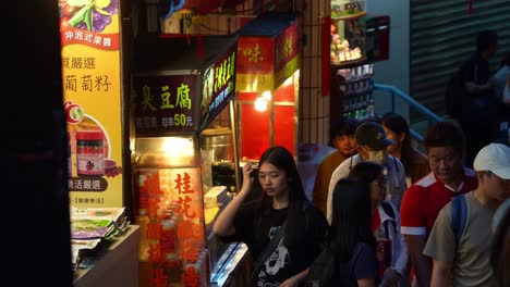 People-strolling-through-Jiufen's-old-street-lined-with-food-stalls-and-souvenir-shops,-exploring-the-charming-mountain-village-town-at-night,-popular-tourist-attraction-of-Taiwan