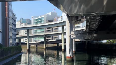 Underneath-a-city-bridge,-sunlit-waterway,-urban-architecture-and-reflections,-clear-day