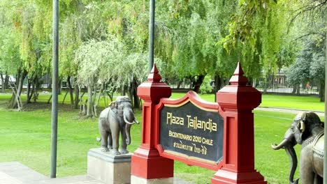 Señal-De-Entrada-A-Plaza-Tailandia-Con-Estatuas-De-Elefantes,-Zona-Verde-Urbana-De-Santiago-De-Chile,-Parque-Araucano