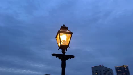 Lámpara-De-Calle-Brillante-Contra-El-Cielo-Crepuscular,-Silueta-De-La-Ciudad-En-El-Fondo,-Ambiente-Nocturno-Tranquilo
