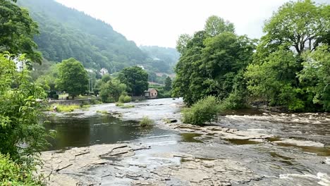 Ein-Wunderschönes-Zeitlupenvideo-Des-Flusses-Dee,-Der-An-Einem-Nebligen-Sommermorgen-über-Das-Felsige-Bett-In-Llangollen-Fließt