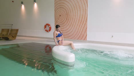Attractive-woman-in-bikini-sits-on-edge-of-bubbling-heated-hotel-pool