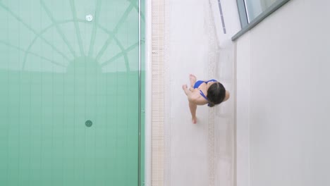 Top-down-aerial-tracking-view-of-fit-woman-in-bikini-walking-next-to-indoor-pool