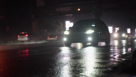 Cámara-Lenta,-Automóviles-Conduciendo-En-El-Tráfico-Húmedo-De-La-Temporada-De-Lluvias,-Camino-Por-La-Noche-Camino-Asfaltado-Iluminado