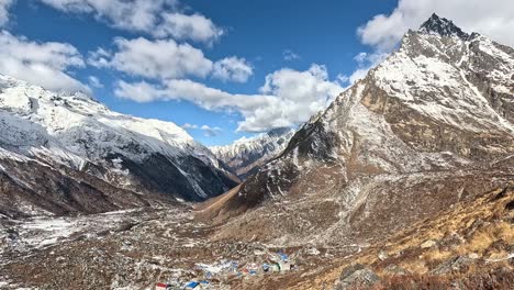 Overlooking-the-expansive-valley-from-Kyanjin-Ri,-featuring-the-quaint-Kyanjin-Gompa-village-nestled-below-Langtang-Lirung’s-snowy-summits,-highlighted-by-patches-of-arid-grass