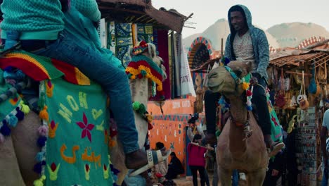Los-Jinetes-De-Camellos-Conducen-Camellos-Vestidos-Coloridamente-En-La-Calle-Del-Mercado-De-La-Aldea-De-Nubia,-Asuán,-Egipto
