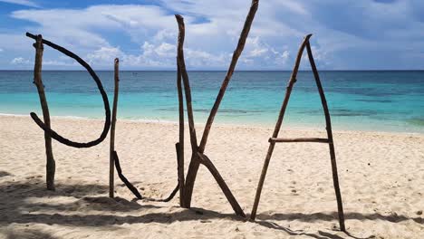 Puka-Shell-Beach-Sign-Made-From-Tree-Branches-on-White-Sand,-Boracay-Island,-Philippines,-Close-Up