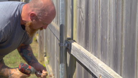 Sweaty-worker-guiding-screw-into-fence;-slow-motion