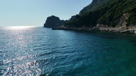 Rotes-Boot,-Das-An-Einem-Sonnigen-Tag-An-Der-üppigen-Küste-Der-Insel-Korfu-Entlangsegelt,-Klares,-Blaues-Ionisches-Meerwasser