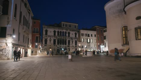 Serena-Plaza-Veneciana-Iluminada-Al-Anochecer,-Exhibiendo-Arquitectura-Clásica-Y-Una-Animada-Multitud-Nocturna.