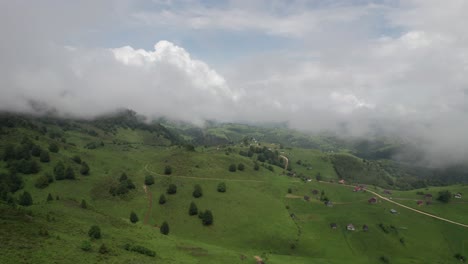 A-lush-green-valley-with-houses-dotted-under-moving-clouds,-aerial-view