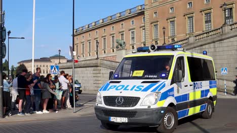 Swedish-police-van-in-motion-with-tourists-by-Stockholm-Palace-in-sunlight,-slow-motion