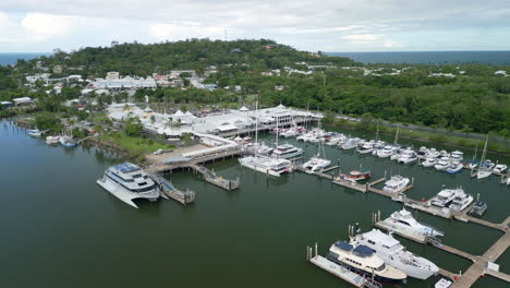 Aerial-drone-fly-near-yacht-cruising-vessels-in-Port-Douglas-Australia-water-bay-port-around-forested-area,-skyline-background-at-daylight