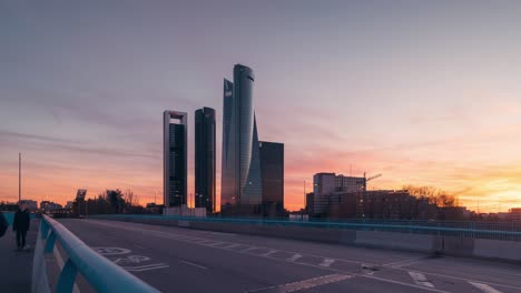 Timelapse-of-Madrid-skyscrapers-CTBA-Cinco-Torres-Business-area-during-colorful-sunset-day-to-night-diagonal-road-and-cars-as-foreground-skyline-towers-background