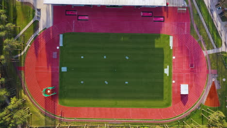 Aerial-bird's-eye-view-of-multi-purpose-stadium-field-with-shadow-from-bleachers,-Valmiera-Latvia