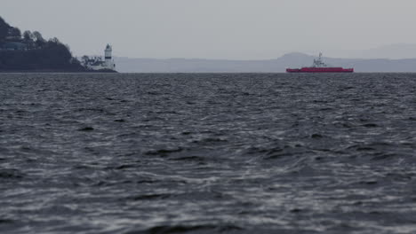 Low-angle-telephoto-view-of-tug-boat-approaching-lighthouse-on-corner