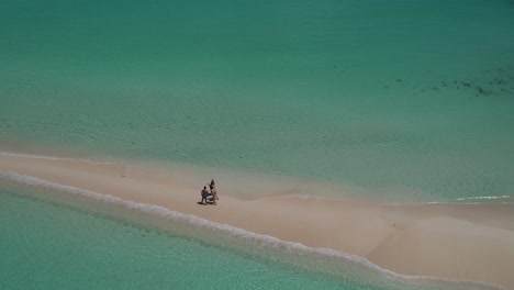 Three-people-walking-on-a-pristine-sandy-beach-in-cayo-de-agua,-los-roques,-venezuela,-turquoise-waters,-aerial-view